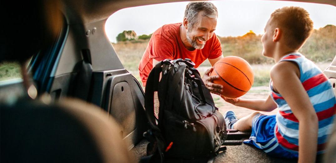 A father and son grab their basketball gear from the back of an SUV.